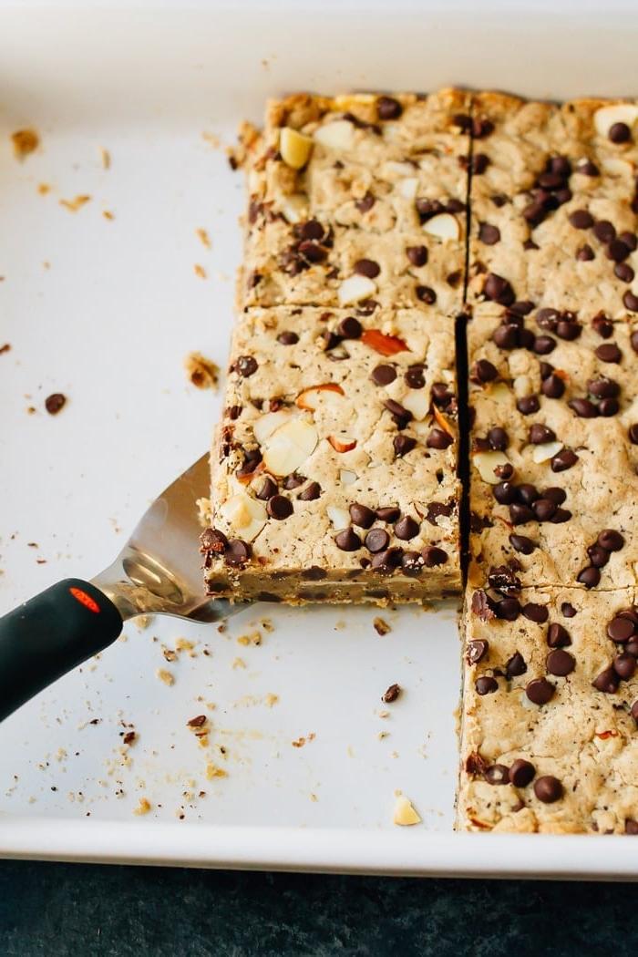 Καταπληκτικές Βίγκαν Μπάρες Καφέ Τόφι 2 Spatula under a cookie bar in a baking pan. The cookie bar is topped with almonds and mini chocolate chips.