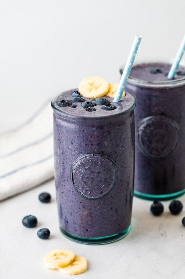 Μύρτιλο Σμούθι 2 Smoothie με μύρτιλα σε ποτήρι, διακοσμημένο με μύρτιλα, φέτες μπανάνας και καλαμάκι.