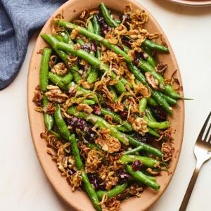 Φασολάκια Σαλάτα 11 An overhead photo looking down onto a serving dish containing green bean salad topped with fried shallots. A fork is resting next to the serving dish, as well as a blue linen dishcloth.
