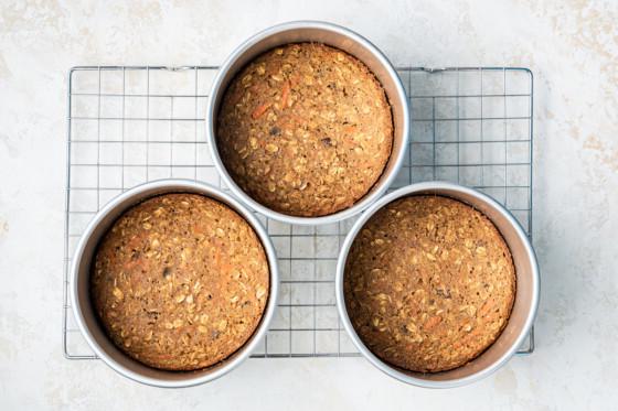 3 6" oatmeal carrot cakes cooling in the pans sitting on a wire rack.