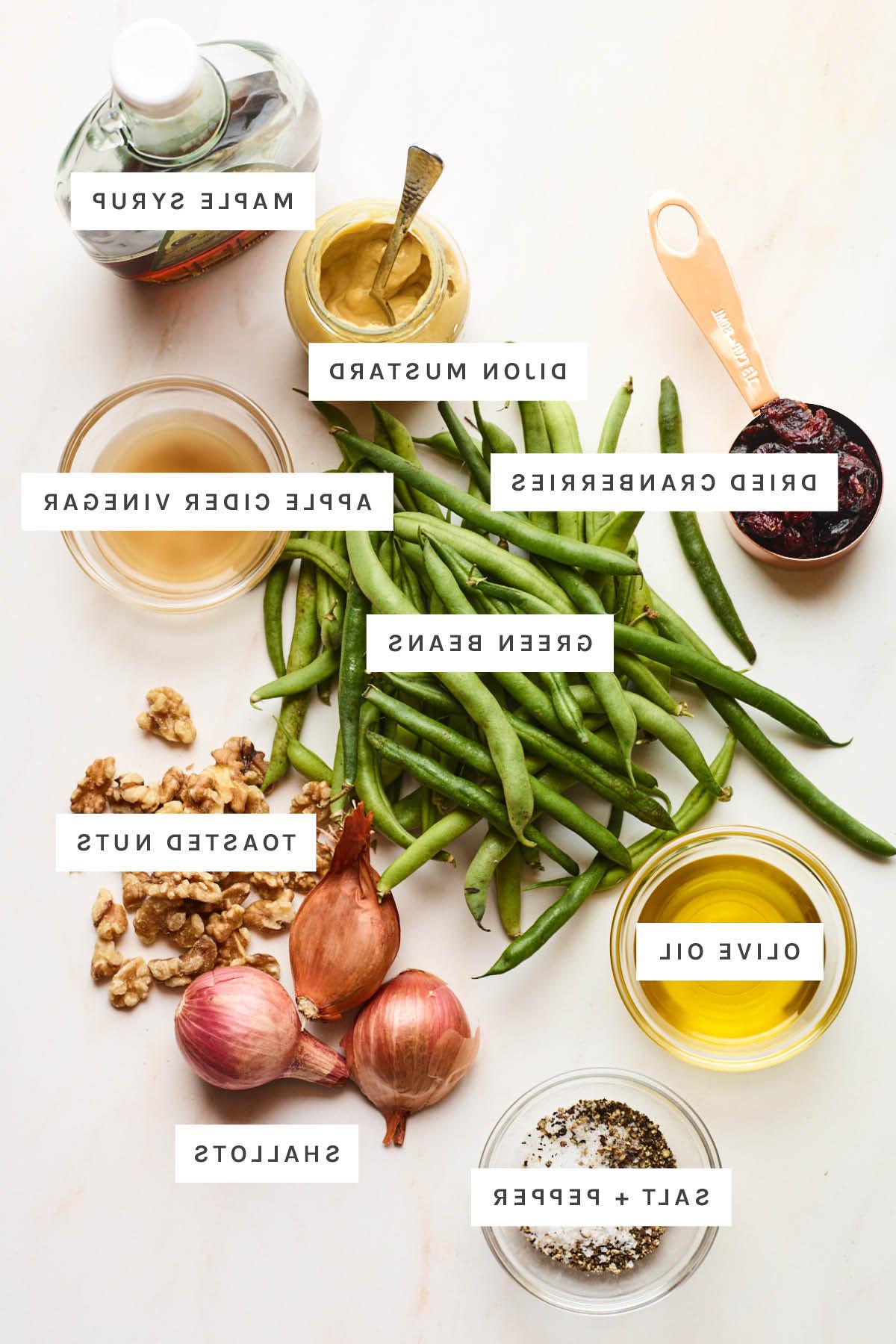 Φασολάκια Σαλάτα 3 Ingredients measured out to make a green bean salad: maple syrup, dijon mustard, apple cider vinegar, dried cranberries, green beans, toasted nuts, olive oil, shallots, salt and pepper.