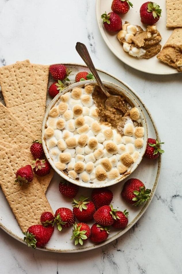 Υγιεινό Σμορς Ντιπ 5 S'mores dip σερβιρισμένο με φράουλες και μπισκότα γκράχαμ για βούτηγμα. Ένα κουτάλι παίρνει μια μερίδα από το ντιπ.