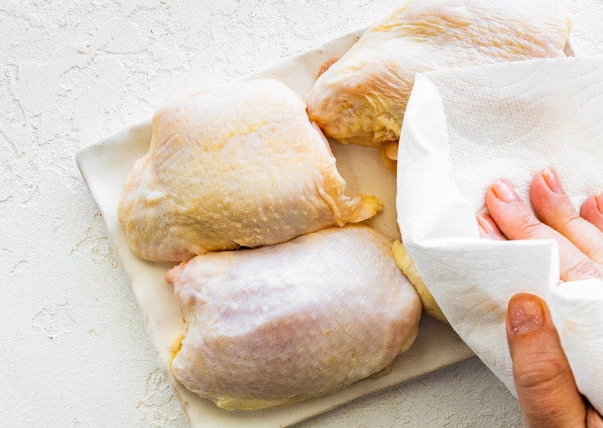 Μπούτια κοτόπουλου στην φριτέζα αέρος 5 Ένα γυναικείο χέρι στεγνώνει τέσσερα μπούτια κοτόπουλου με κόκαλο με χαρτί κουζίνας.