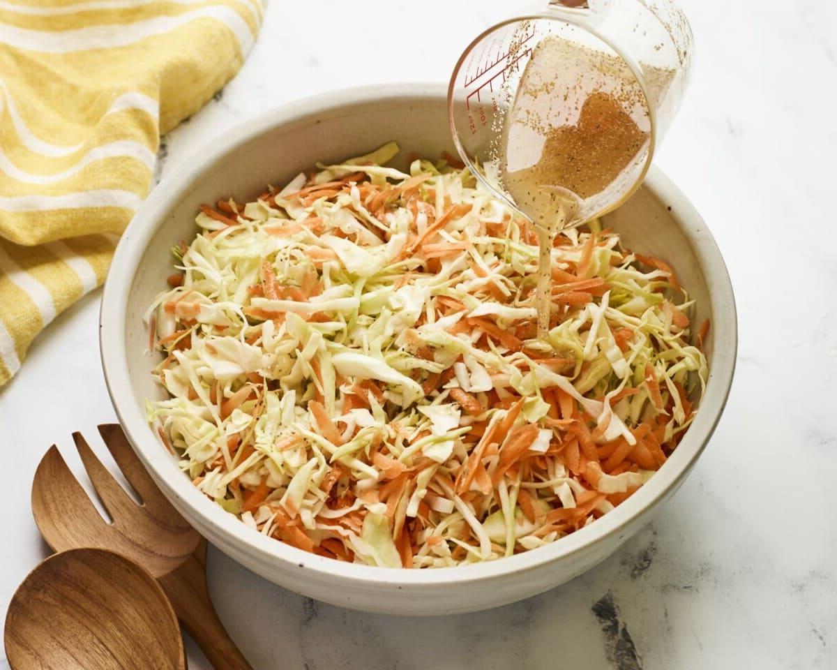 Ξιδάτο Κόλσλοου 5 Ρίχνοντας ξιδάτο dressing μήλοξυδου πάνω από μπολ σερβιρίσματος με λαχανοσαλάτα.