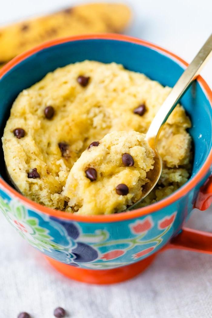 Καρυδόλευρο Κέικ Κούπας 5 Mug with a chocolate chip mug cake and a spoon scooping out a bite.