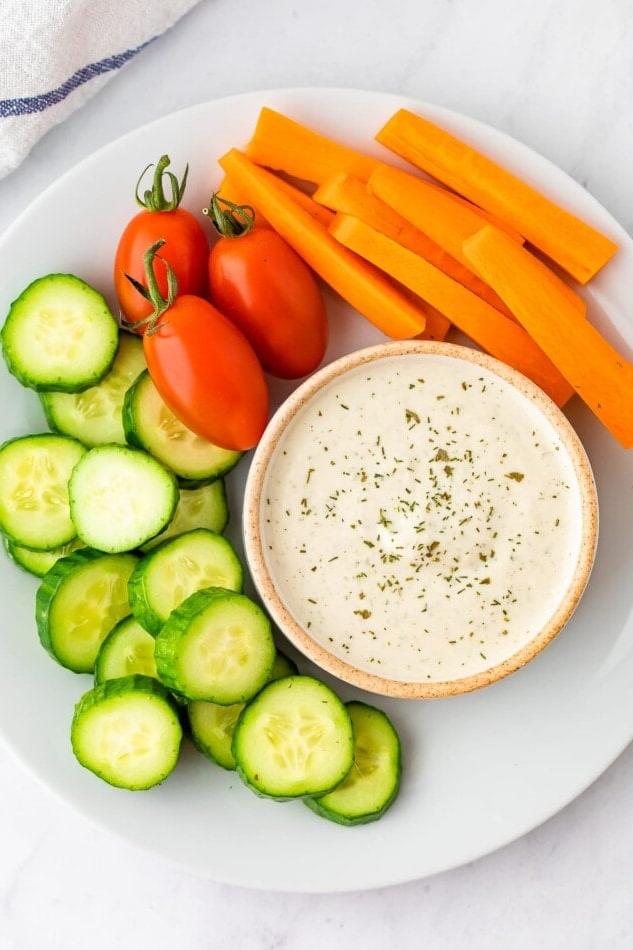 Βίγκαν Ραντς Σάλτσα 6 Βίγκαν ranch σε ένα μικρό μπολ με φρέσκα λαχανικά γύρω του για ντιπάρισμα. Όλα σε ένα λευκό πιάτο.