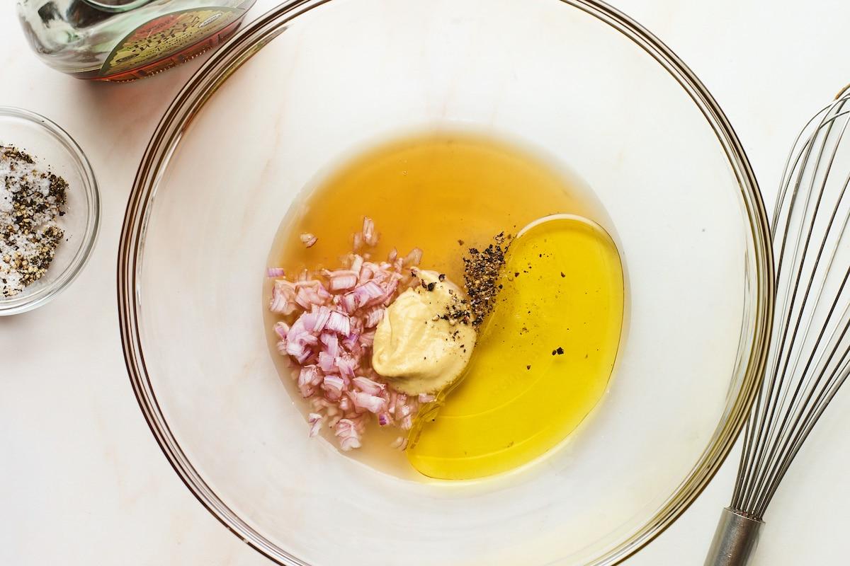 Φασολάκια Σαλάτα 6 A glass mixing bowl containing apple cider vinegar, olive oil, maple syrup, minced shallots, dijon mustard, sea salt and pepper.