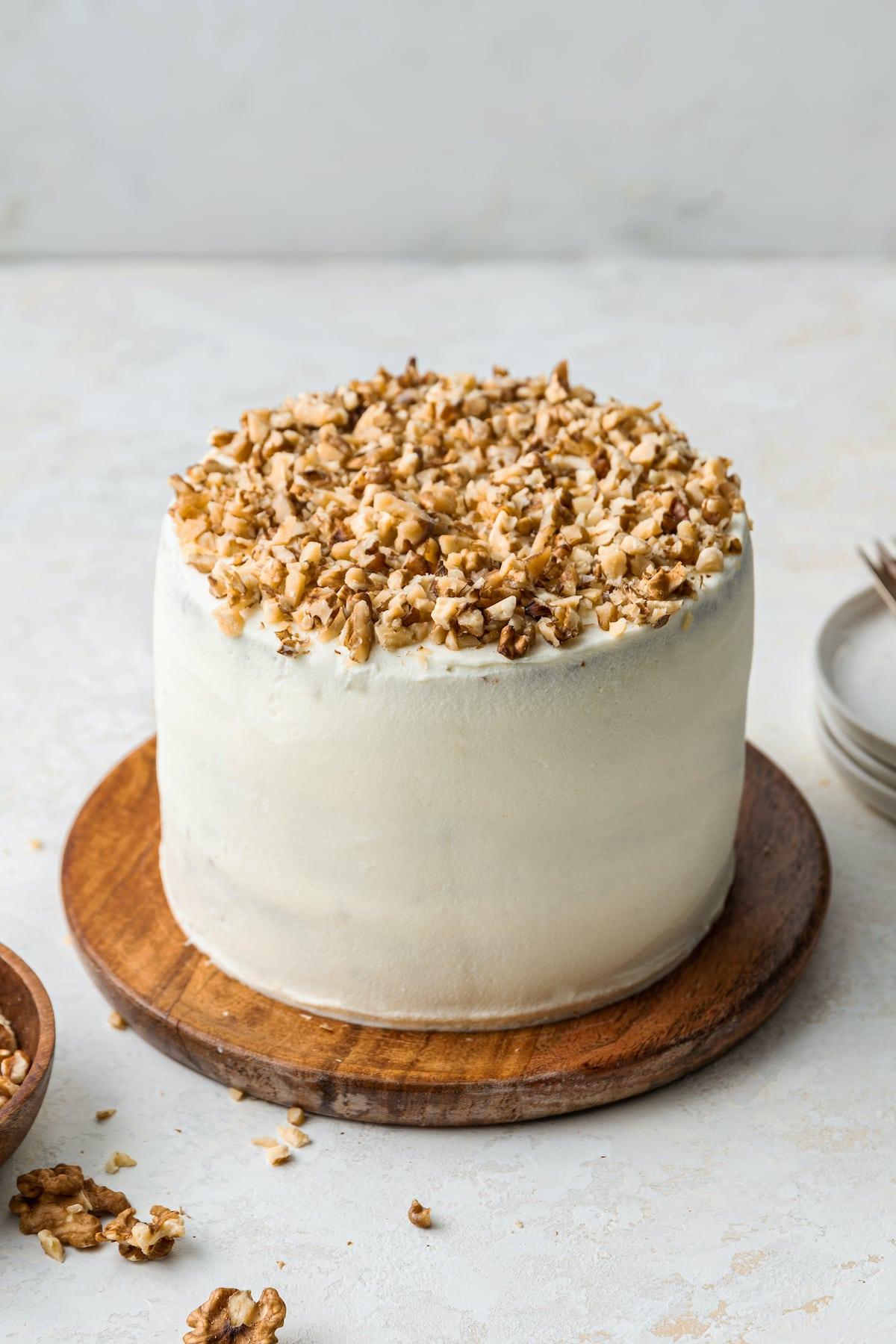 Κέικ βρώμης και καρότου 8 A fully frosted 3-layer oatmeal carrot cake topped with chopped walnuts and served on a wooden board.