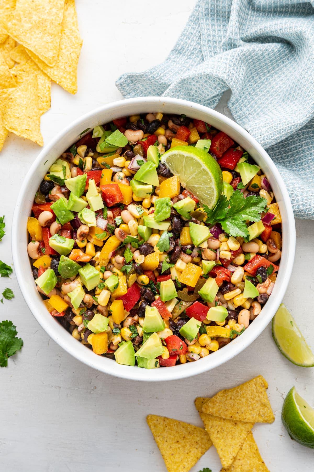 Καουμπόι Χαβιάρι 11 Ένα μπολ με σαλάτα Cowboy Caviar με κομμένο αβοκάντο, μια φέτα λάιμ και τσιπς τορτίγιας στο πλάι.