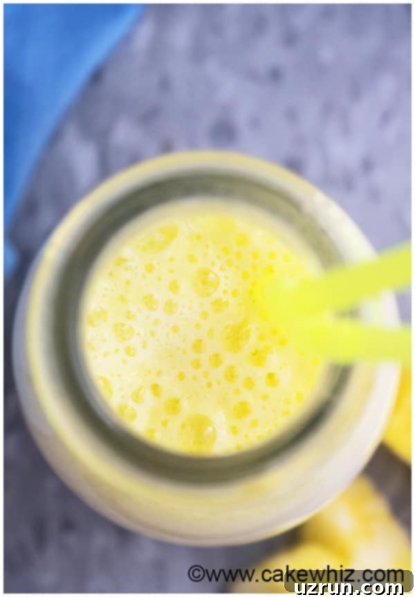 Simple Pineapple Smoothie Banana Free 3 Overhead Shot of Bubbles in Glass of Yellow Smoothie.