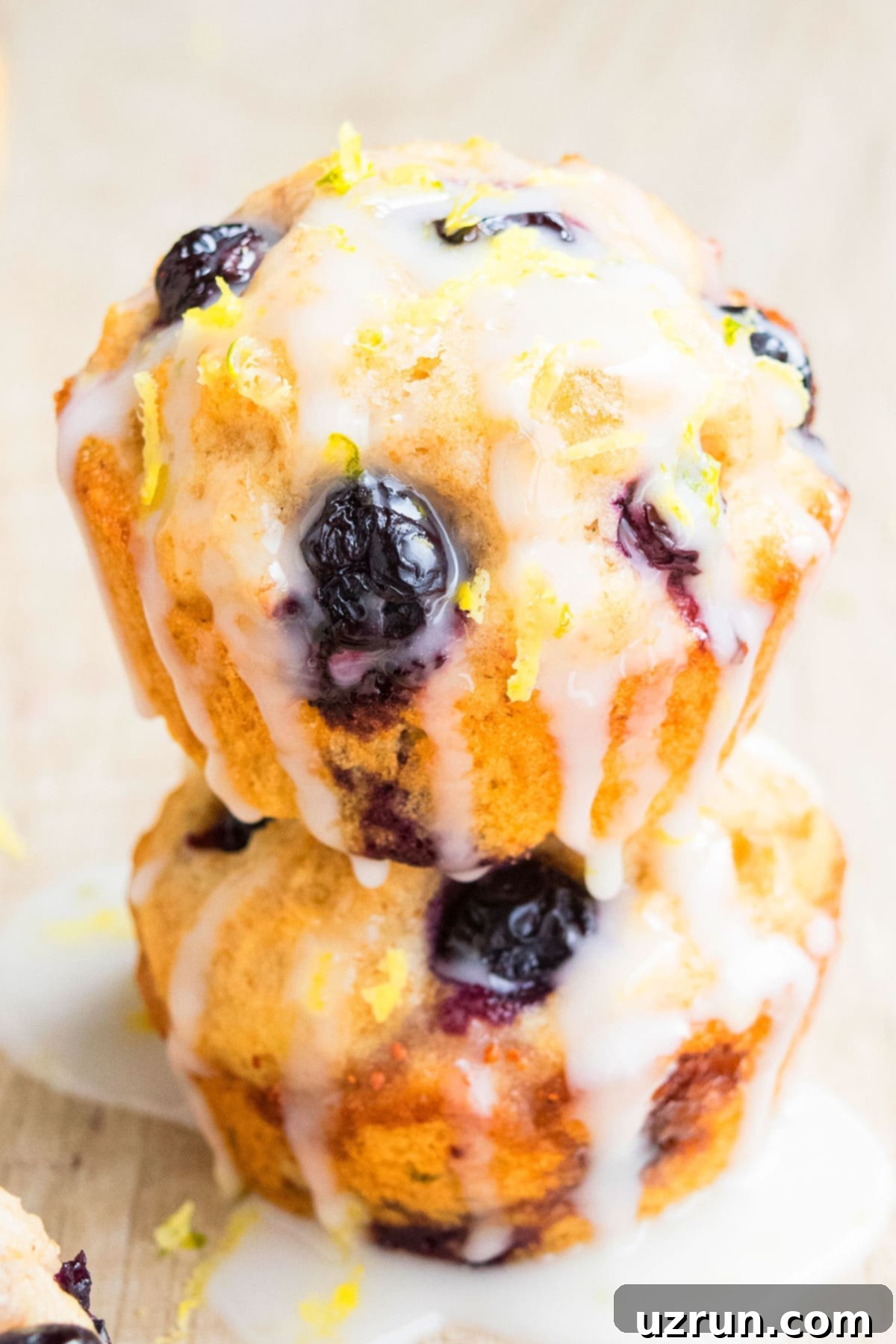Glazed Lemon Blueberry Muffins 3 Stack of Glazed Muffins on Light Brown Background.