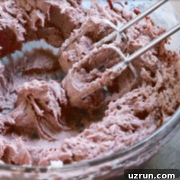 Effortless Blackberry Buttercream Frosting 9 Hand held mixer being used to mix ingredients in glass bowl.