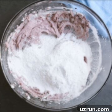 Effortless Blackberry Buttercream Frosting 6 Powdered sugar added to mixture in glass bowl.