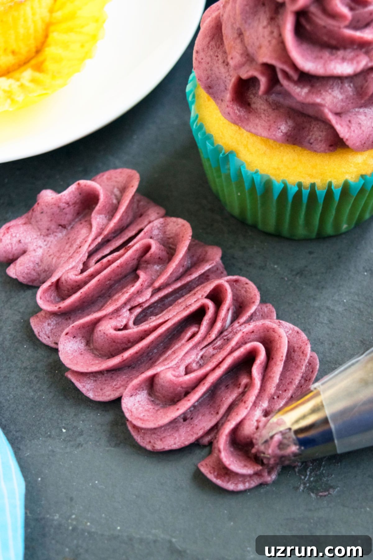 Effortless Blackberry Buttercream Frosting 10 Fresh Blackberry icing piped on rustic gray dish with a piping bag.
