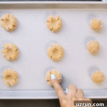 Easy Peanut Butter Blossoms with Hershey's Kisses 11 Cookie dough balls being indented in the center before baking.