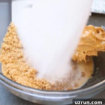 Easy Peanut Butter Blossoms with Hershey's Kisses 5 Glass bowl with coconut oil, peanut butter, vanilla extract, milk, brown sugar, granulated sugar.