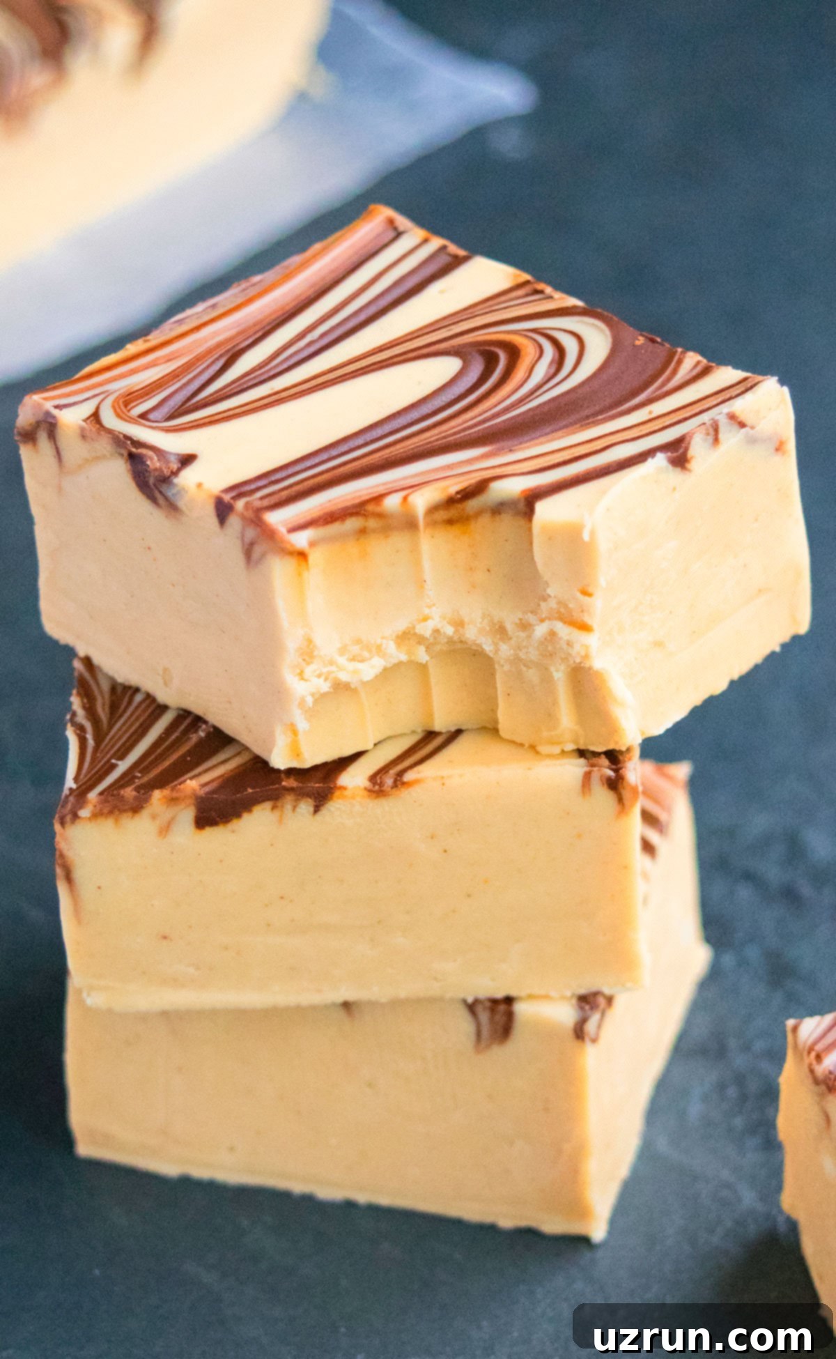 Chocolate Peanut Butter Swirl Fudge 3 Stack of Fudge Slices With One on Top That's Partially Eaten on Dark Gray Background.