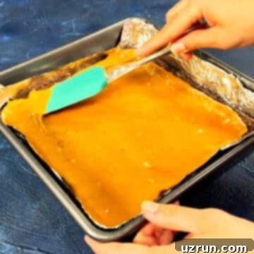 Five-Layer Chocolate Cookie Bars 6 Melted caramel being spread on top of baked cookie base.