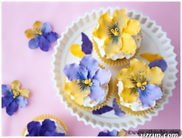 Easy Fondant Pansy Cupcakes 3 Easy Homemade Floral Cupcakes on White Cake Stand with Pink Background, showcasing delicate pansy toppers