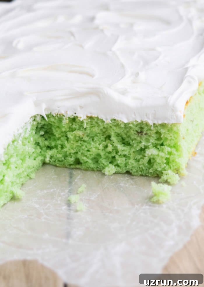 Effortless Pistachio Cake 4 Closeup Shot of Green Cake With Whipped Cream on Parchment Paper, ready to be served