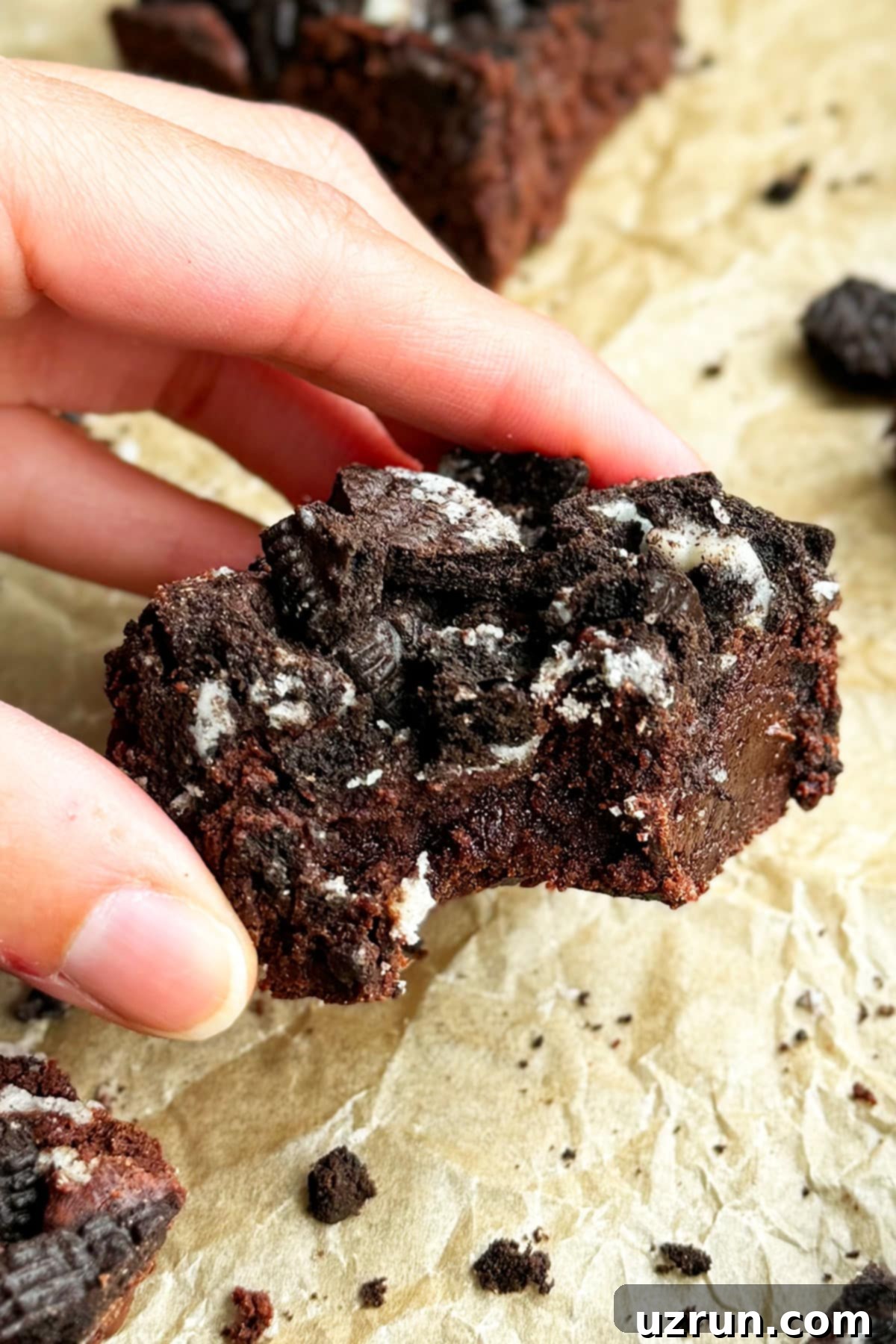 Easy Fudgy Oreo Brownies 12 Fingers holding a partially eaten fudgy Oreo brownie, highlighting its appealing texture.