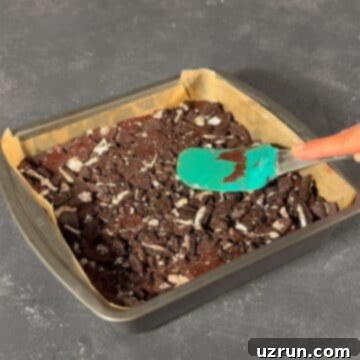 Easy Fudgy Oreo Brownies 10 Brownie batter being pressed with crushed Oreo cookies using a spatula.