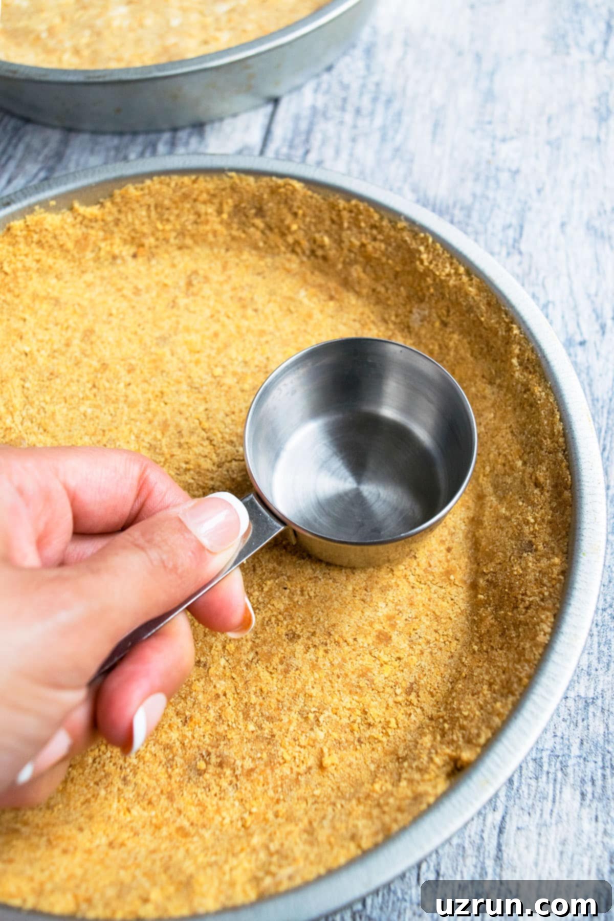 Easy No-Bake Graham Cracker Crust 4 Flattening Graham Cracker Crumbs in Pan With a Flat Based Measuring Cup.