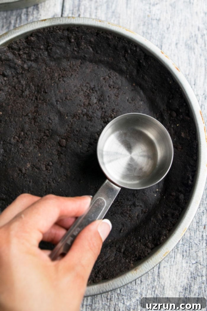 No-Fuss No Bake Oreo Pie Crust 3 Measuring Cup Being used to Pack Down Cookie Crumbs into an Oreo pie crust.