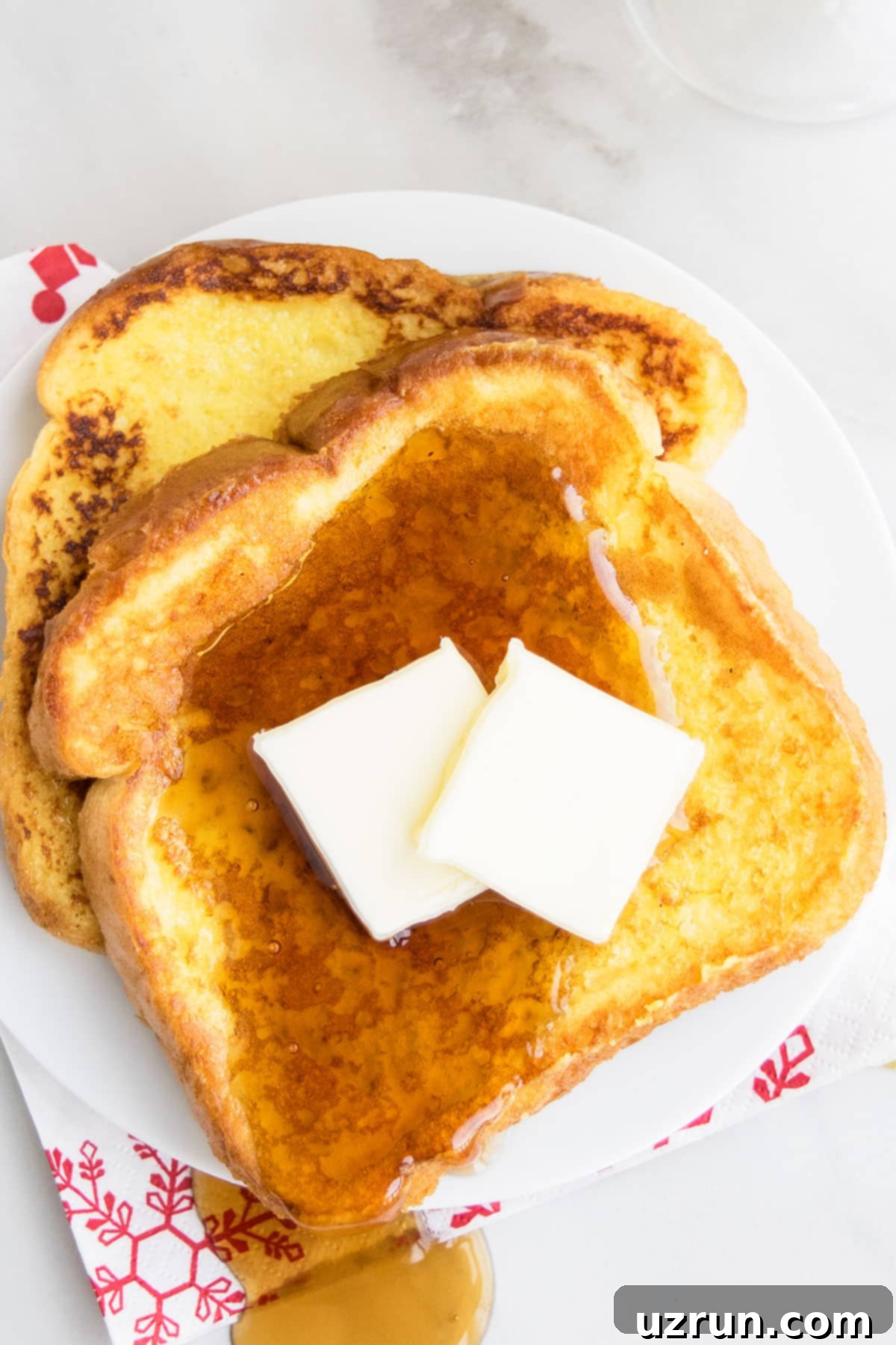 Slices of Easy Eggnog French Toast With Maple Syrup and Butter on White Dish. 