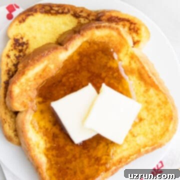Perfect Easy Eggnog French Toast 5 Slices of Easy Eggnog French Toast With Maple Syrup and Butter on White Dish.