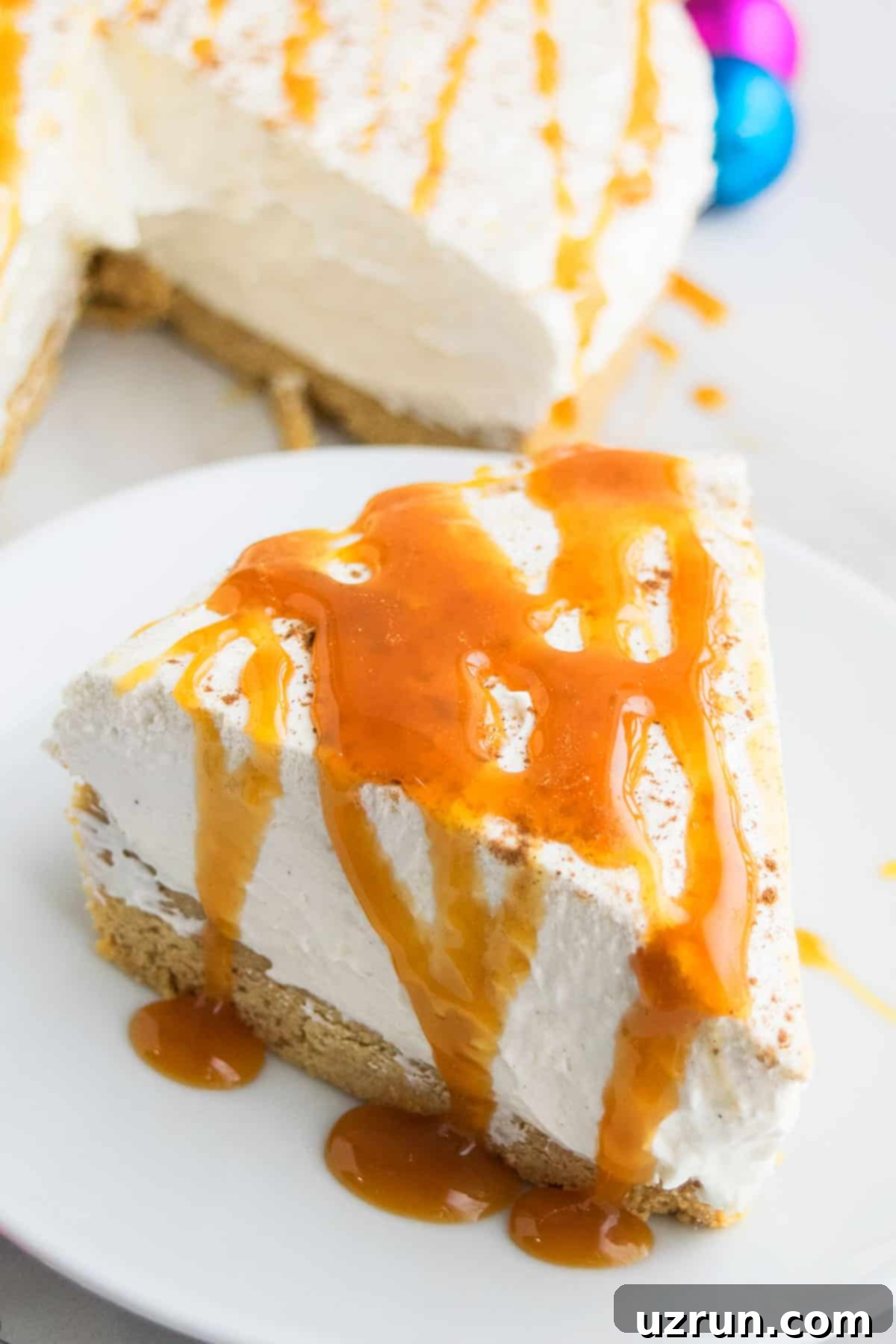 A perfect slice of creamy No Bake Eggnog Cheesecake, elegantly topped with a caramel drizzle and a sprinkle of nutmeg, served on a white dish against a festive backdrop.