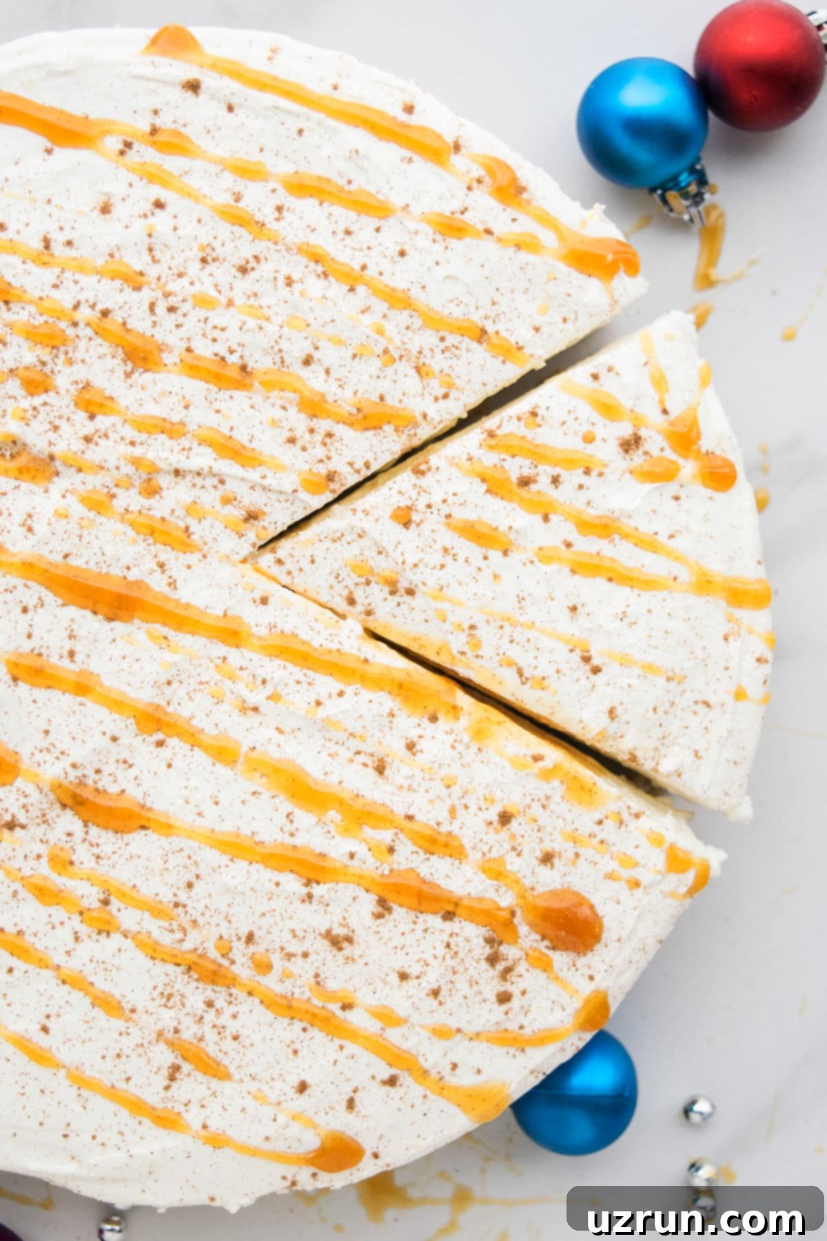 No-Bake Eggnog Cheesecake 3 An overhead shot showcasing a whole No Bake Eggnog Cheesecake, adorned with caramel sauce and nutmeg, presented on a white marble background with festive holiday decorations.