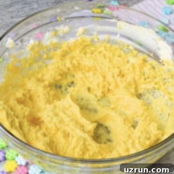 Easy Mango Buttercream Frosting 7 Mango puree mixed with butter mixture in glass bowl.