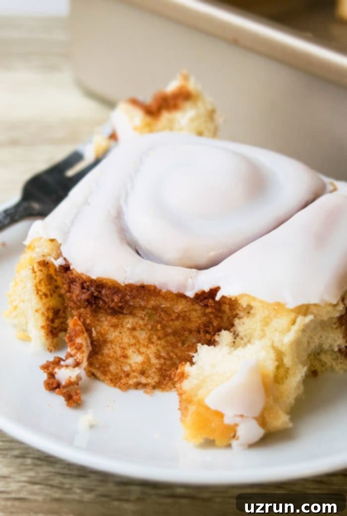 Foolproof One-Hour Homemade Cinnamon Buns 4 Partially Eaten Glazed Yeast Rolls on White Dish.