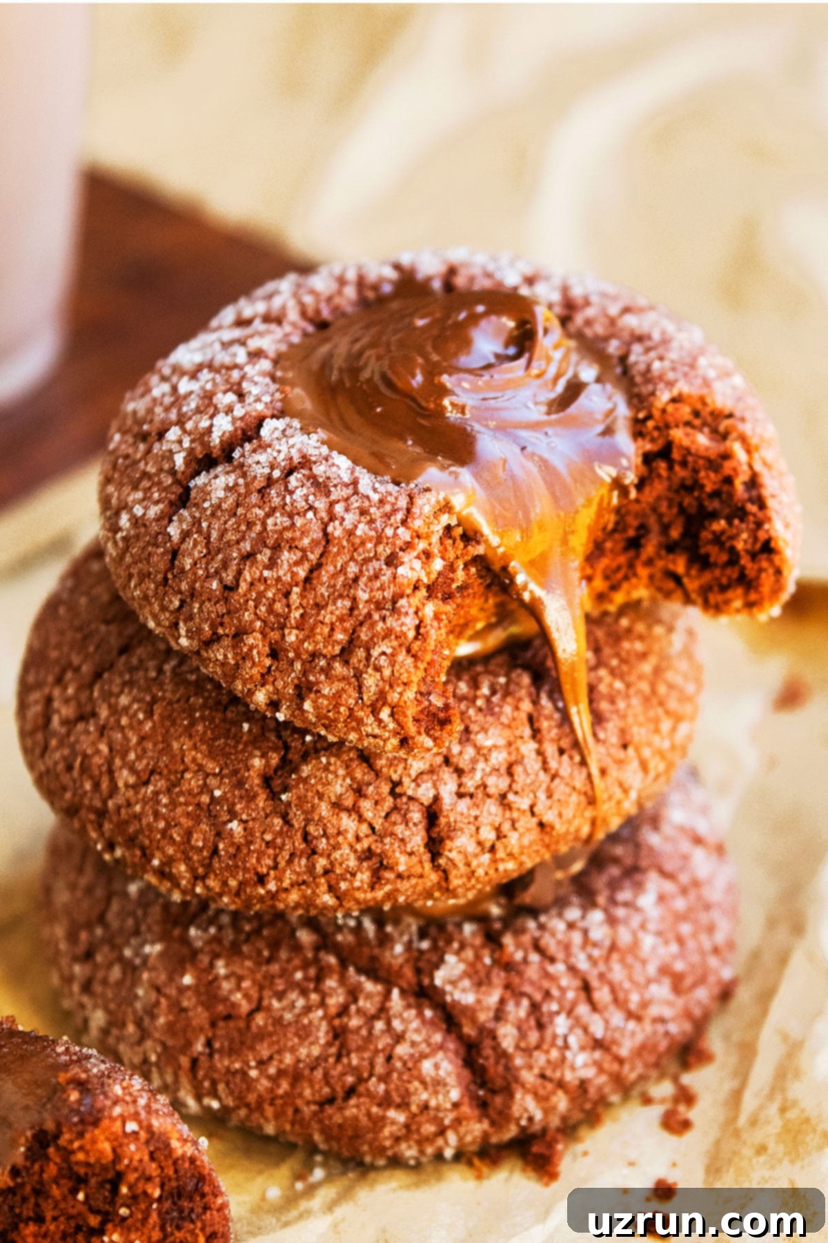 Stack of Chocolate Thumbprint Cookies With Ganache Filling on Brown Parchment Paper, showcasing their rich color and inviting texture.