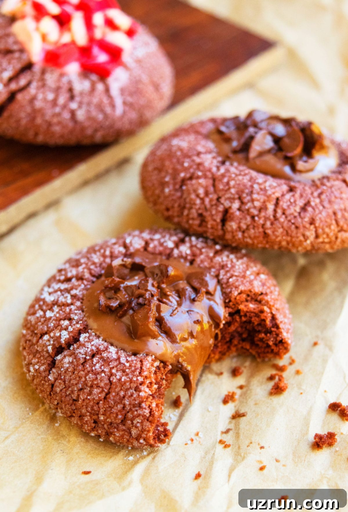 Ganache-Filled Chocolate Thumbprint Cookies 3 Partially Eaten Chocolate Thumbprint Cookie on Brown Parchment Paper, showing the soft interior and ganache filling.