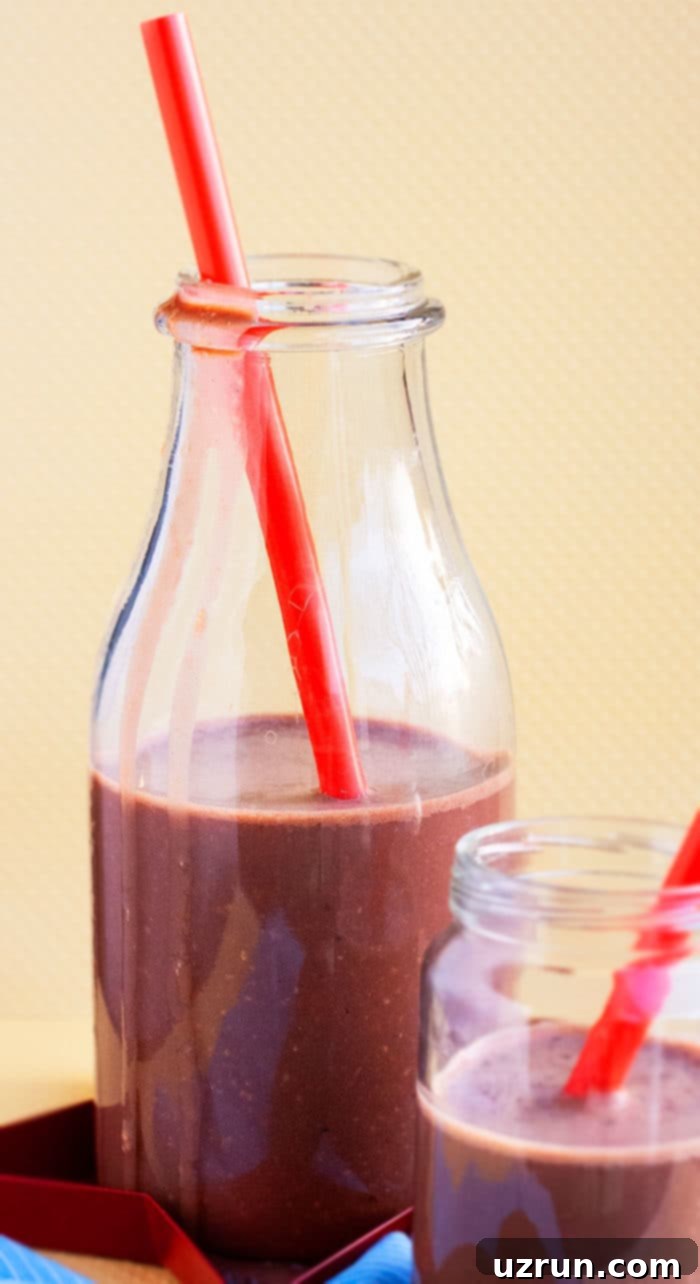 Creamy Chocolate Peanut Butter Banana Smoothie in a glass with a red straw, garnished with banana slices and chocolate chips