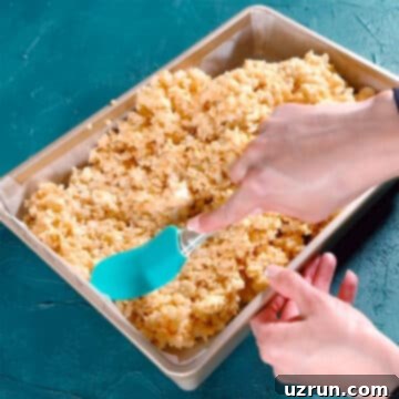 The Ultimate Guide to Perfect Rice Krispie Treats 9 Sticky rice krispies mixture being spread in a rectangle pan with rubber spatula.
