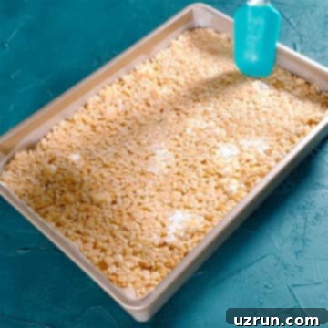 The Ultimate Guide to Perfect Rice Krispie Treats 10 Marshmallow mixture in rectangle pan being flattened with rubber spatula.