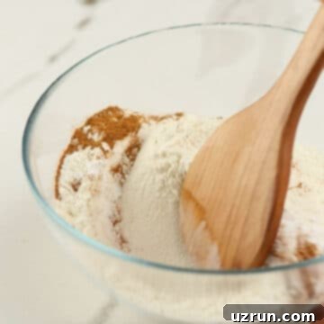 Baked Apple Cider Cake Donuts 6 Wooden spoon being used to mix flour, spices and leavening agents in glass bowl.