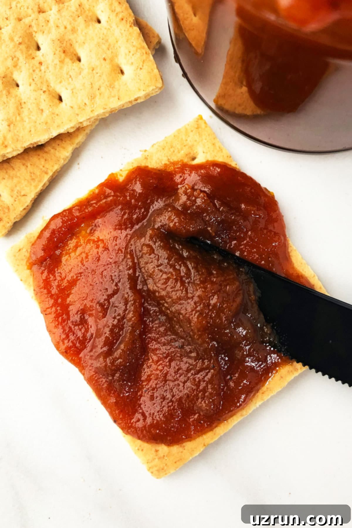 Simple 5-Ingredient Crockpot Pumpkin Butter 4 Graham Cracker With Pumpkin Spread on Marble White Background.