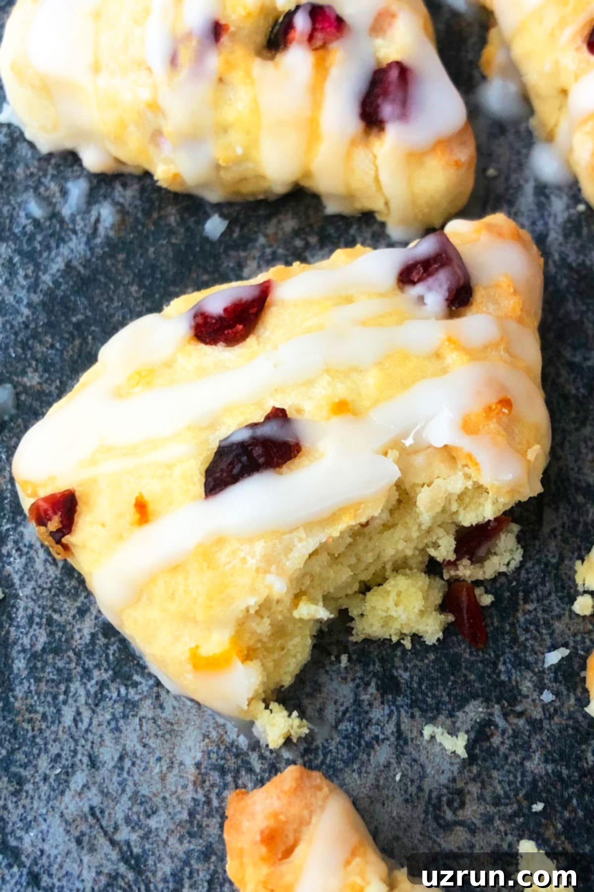Effortless Glazed Cranberry Orange Scones 4 Partially Eaten Scone on Rustic Gray Background.