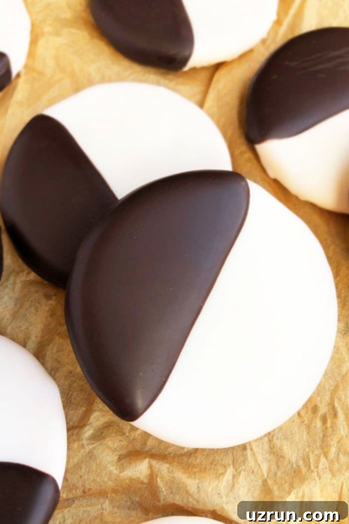 Angled view of a stack of classic NYC Black and White Amerikaners cookies on brown paper, showcasing the iconic half-vanilla, half-chocolate frosting.