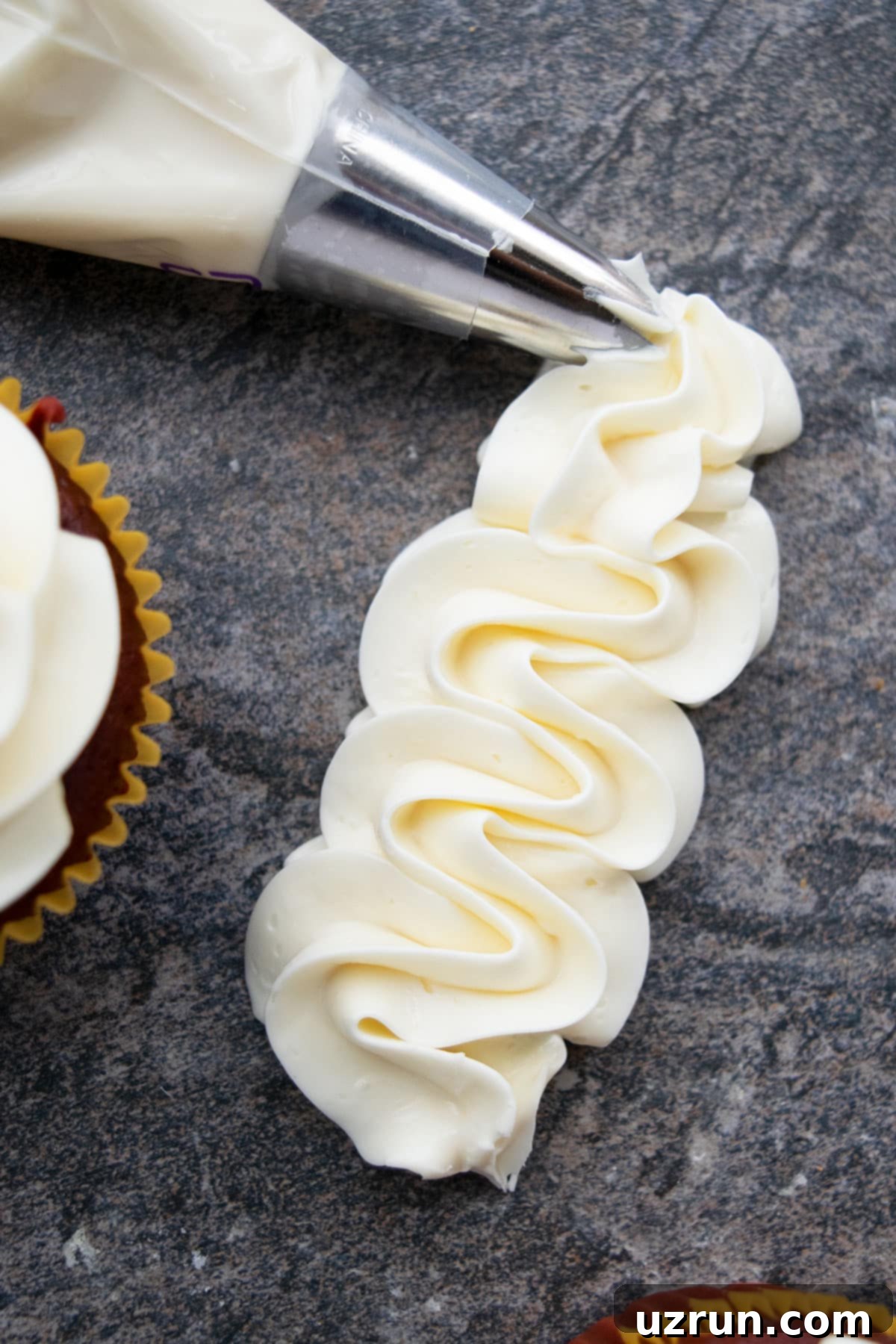Silky Swiss Meringue Buttercream 4 Icing Piped on Gray Background With Piping Bag Nearby.