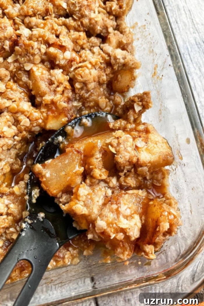 Closeup Shot of Spoonful of Best Caramel Apple Crisp in Glass Dish, showing the gooey apple filling and golden-brown oat topping.
