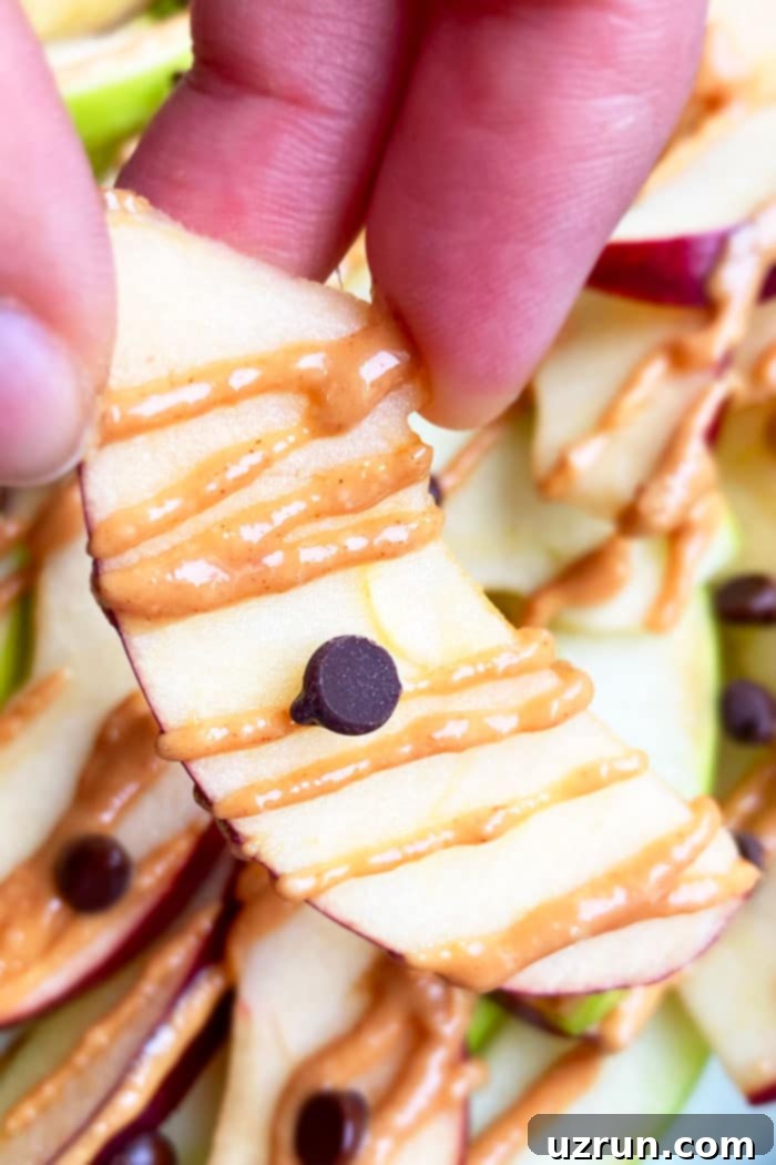 Super Easy Apple Nachos 4 Closeup Shot of Holding an Apple Slice with Peanut Butter and Chocolate Chips