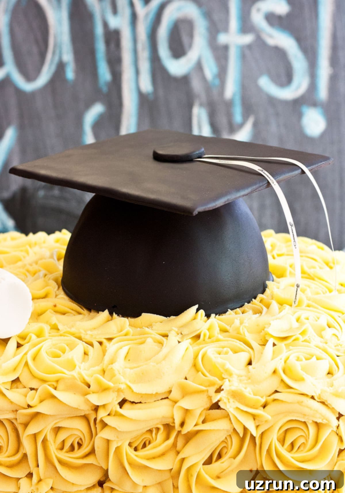 Easy Homemade Graduation Cake Decorated With Fondant Cap and Buttercream Rosettes on Chalkboard Background.