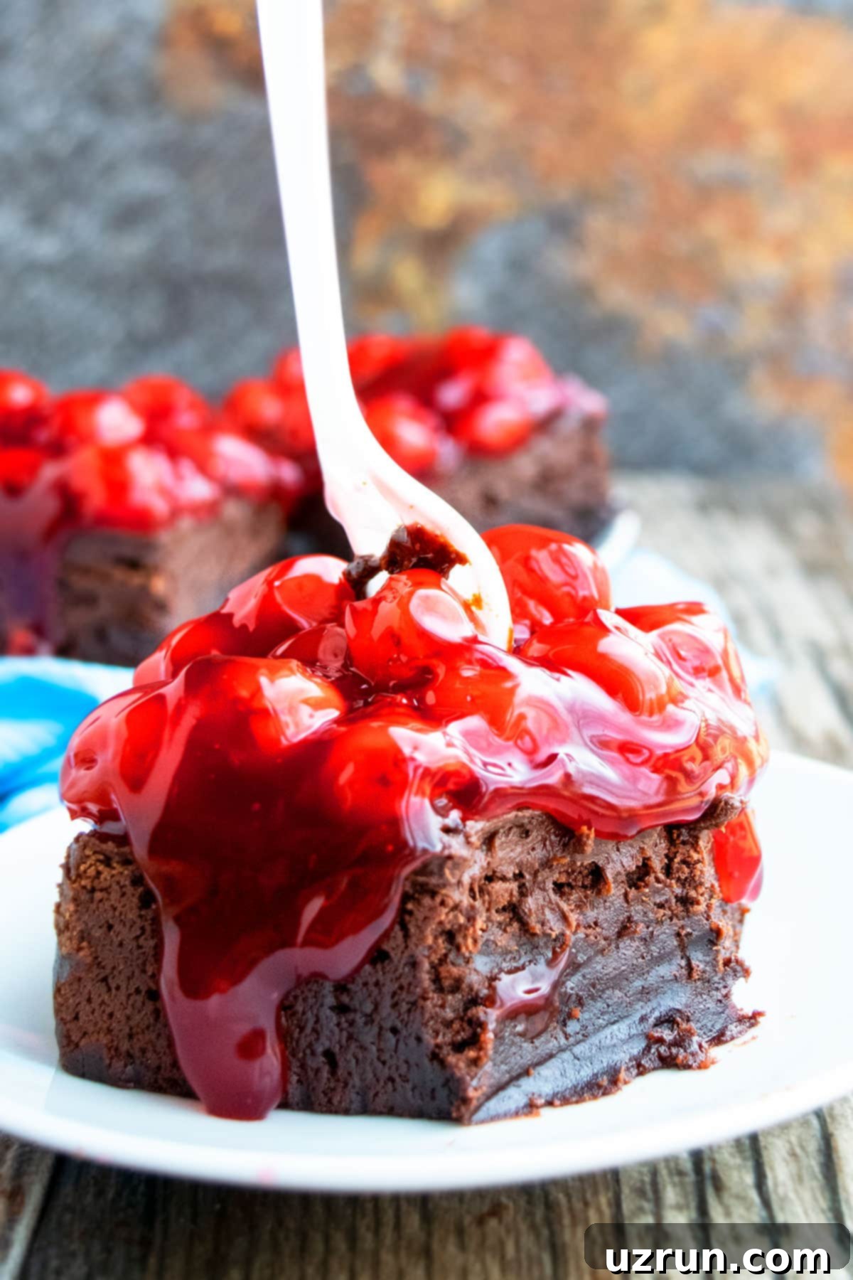 Dark Chocolate Cherry Fudge Brownies 3 Homemade Fudgy Frosted Chocolate Cherry Brownies on White Plate With Fork Pushed Through the Center.