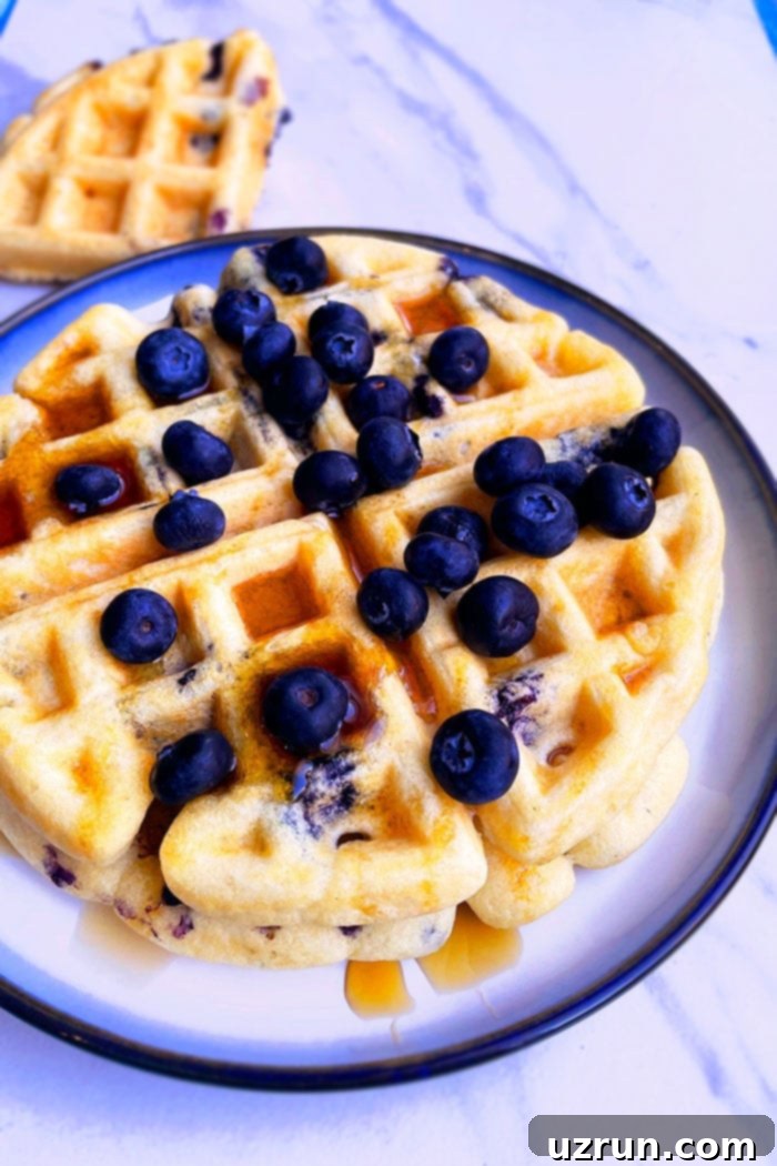 Stack of Easy Homemade Blueberry Waffles on White Plate with Light Blue Background
