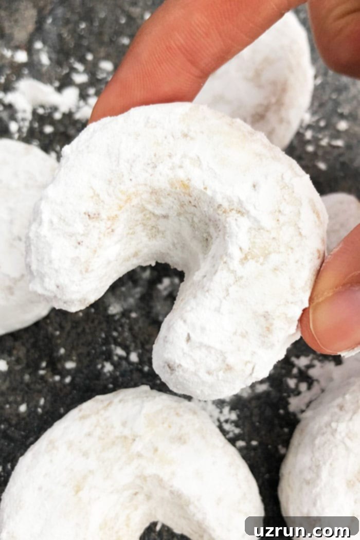 Almond Crescent Cookies 4 Two Fingers Holding Kiperl Cookie Over Grayish Black Background